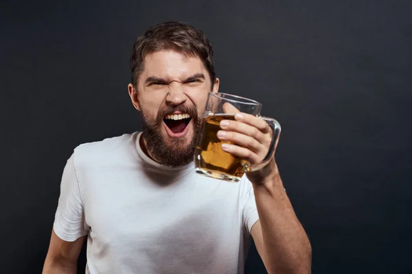 Homme avec une tasse de bière dans ses mains émotions style de vie amusant t-shirt blanc fond sombre isolé — Photo