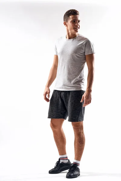 Спортивний чоловік в шортах і повнометражна футболка робить вправи на світлому тлі — стокове фото