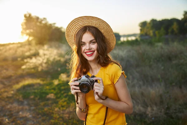 Kadın fotoğrafçı kamera ellerinde gülümsüyor kırmızı dudak şapka çekici görünüm doğa — Stok fotoğraf