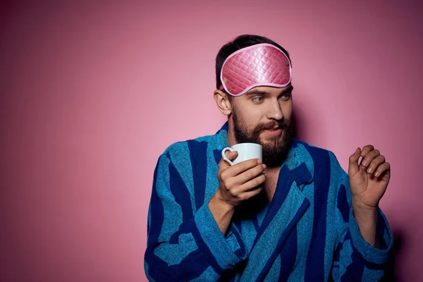 Homem com uma xícara de chá na mão e com uma máscara rosa no rosto em um fundo rosa vista cortada — Fotografia de Stock