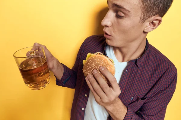 Vrolijke man met een beker bier en een hamburger op zijn handen dieetvoeding levensstijl gele achtergrond — Stockfoto