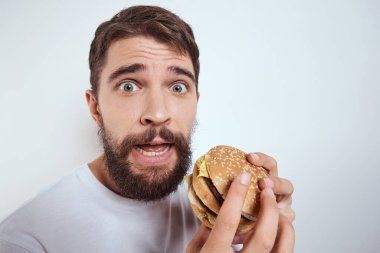 Beyaz bir tişörtle arka planda hamburger yiyen bir adam yakın çekim açlık ve fast food manzarası izledi.