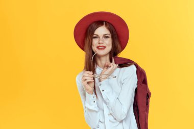 Omuzlarında ceketi olan bir kadın. Kırmızı şapka, beyaz gömlek. Zarif, sarı arka plan.
