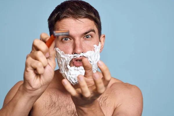 Man met scheermes en wit schuim op zijn gezicht blauwe achtergrond naakt romp baden procedures — Stockfoto