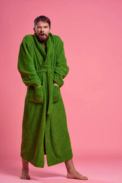 Emocjonalny mężczyzna w zielonym szlafroku w pełnym wzroście na różowym tle gestów z rękami do modelki — Zdjęcie stockowe