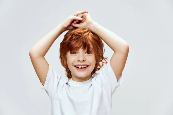 Słodkie ruda chłopiec trzymając ręce na głowa uśmiech zabawa biały t-shirt — Zdjęcie stockowe