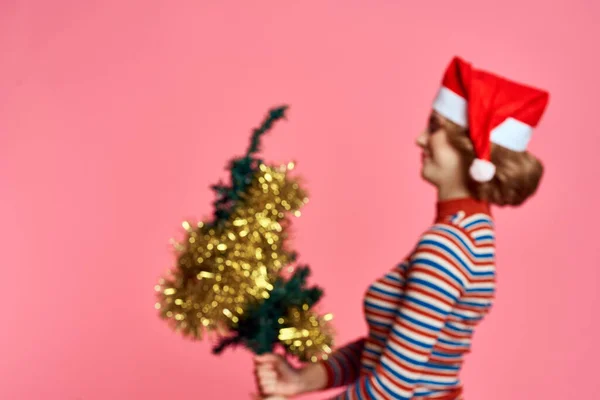 Жінка з різдвяною ялинкою в руках і жовтим червоним шапочкою рожевим фоном — стокове фото