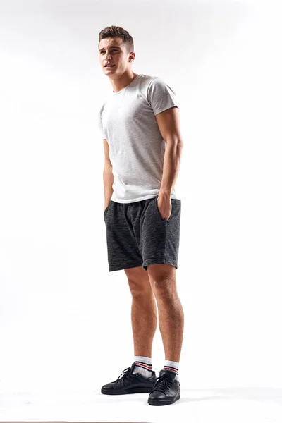 Een sportman in shorts en een full-length T-shirt doet oefeningen op een lichte achtergrond — Stockfoto