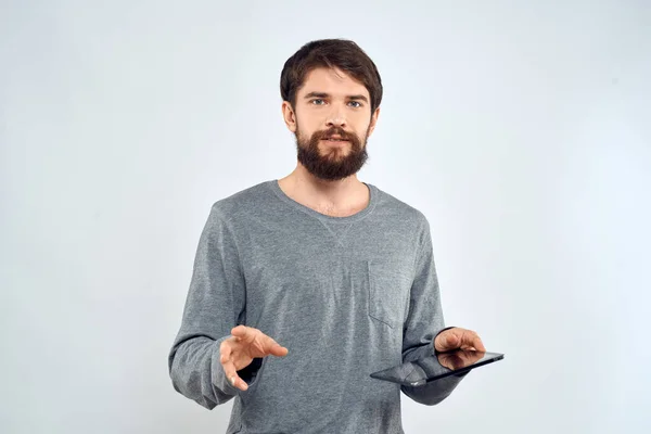 Ένας άνθρωπος σε ένα γκρι πουλόβερ ένα δισκίο στα χέρια των συναισθημάτων Internet τεχνολογία lifestyle φως φόντο — Φωτογραφία Αρχείου
