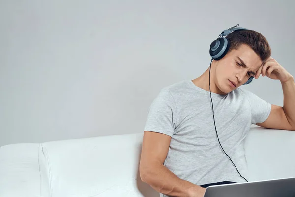 Un uomo sul divano di fronte a un computer portatile con un joystick in cuffie tecnologiche per videogiochi — Foto Stock