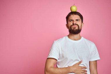 Pembe arka planda elmalı tatlı bir adam. Elleri kesilmiş beyaz tişörtlü, Uzay Kopyası.