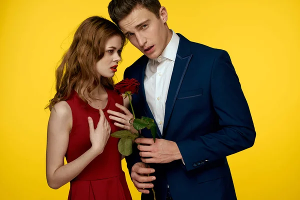 En romantisk man kramar en kvinna i en röd klänning med en ros i handen på en gul bakgrund — Stockfoto