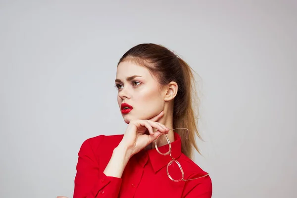 Mujer de moda en una camisa roja sobre un fondo claro emociones divertidas gafas de maquillaje brillantes aspecto atractivo —  Fotos de Stock