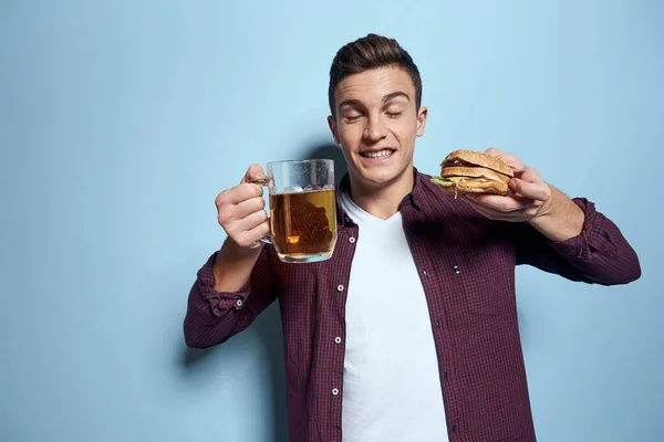 Vrolijk dronken man met bier mok en hamburger in de hand dieet voedsel levensstijl blauwe achtergrond — Stockfoto