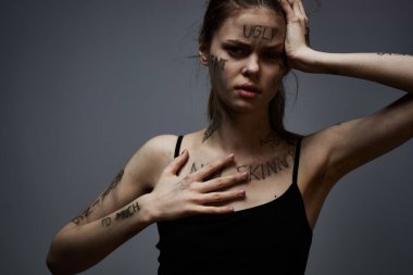 Gri arka planda kırıcı yazılar yazan üzgün kadın elleriyle kendine dokunuyor.