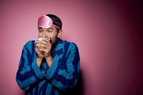 Hombre con una taza de té en la mano y con una máscara rosa en la cara sobre un fondo rosa vista recortada —  Fotos de Stock