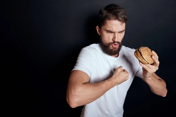Muž jíst hamburger fast food restaurace Gourmet jíst tmavé pozadí — Stock fotografie