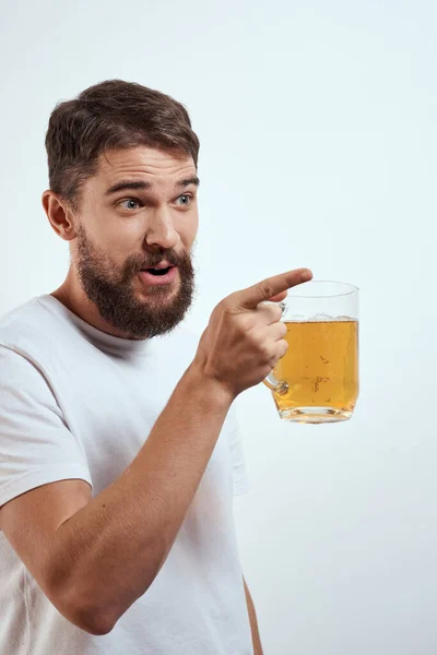 Hombre con una taza de cerveza en sus manos y una camiseta blanca fondo claro bigote barba emociones modelo —  Fotos de Stock