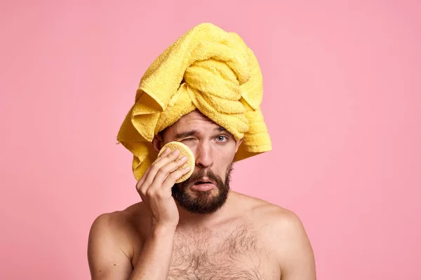 man with yellow towel on his head sponge clean skin care pink background