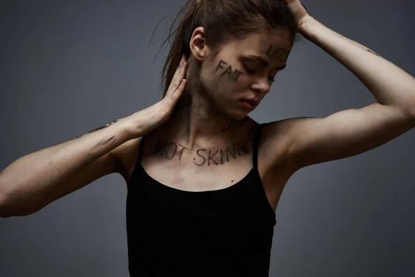 Mulher chateada com escrita ofensiva em seu corpo no fundo cinza tocando-se com as mãos corte vista — Fotografia de Stock