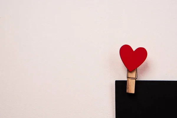Dřevěný kolík na prádlo s červeným srdcem na černém listu papíru a světlým pozadím — Stock fotografie