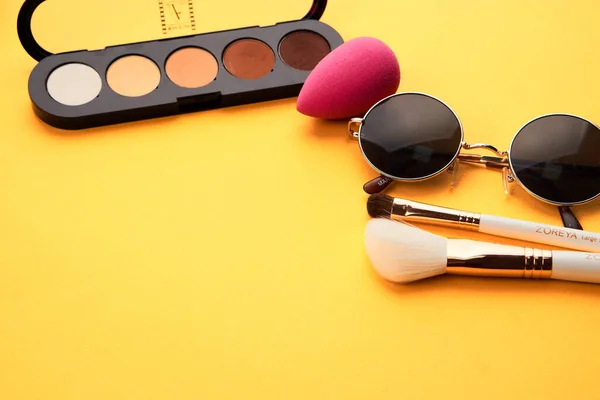 Sombras de ojos sobre un fondo amarillo cosméticos profesionales maquillaje cepillos esponja suave gafas de moda — Foto de Stock