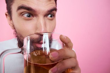 Pembe arka planda büyük bir bardak birayla sarhoş bir adam ve kalın sakallı rahat bir tişört. 