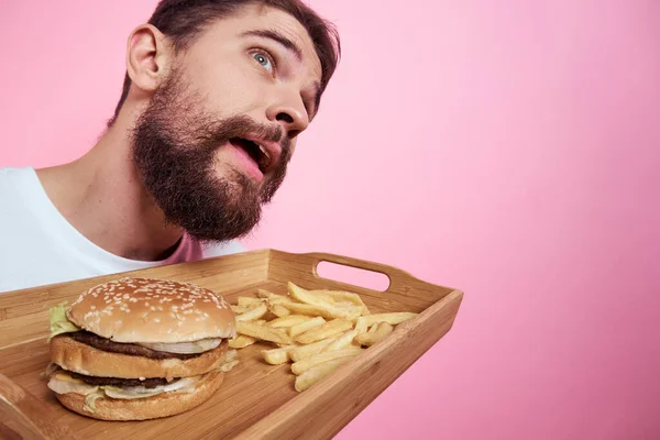 Elinde yemek tepsisi olan bir adam hamburger kızartması ve fast food kalorisi pembe arka plan portresi. — Stok fotoğraf