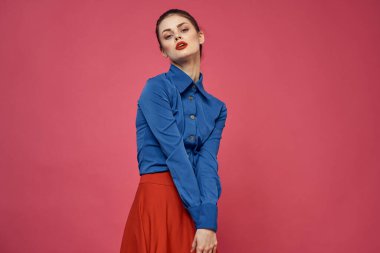 Pembe arka planda mavi gömlekli şık bir kadın. Kırmızı etek duyguları. El hareketleriyle hareket ediyor.