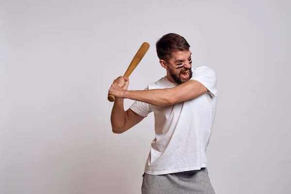 Un uomo emotivo con una mazza da baseball su uno sfondo chiaro in una t-shirt bianca sta gesticolando con le mani al modello — Foto Stock