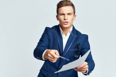 Ceketli bir iş adamı, elinde belgelerle arka planda hafif bir iş üzerinde çalışıyor.