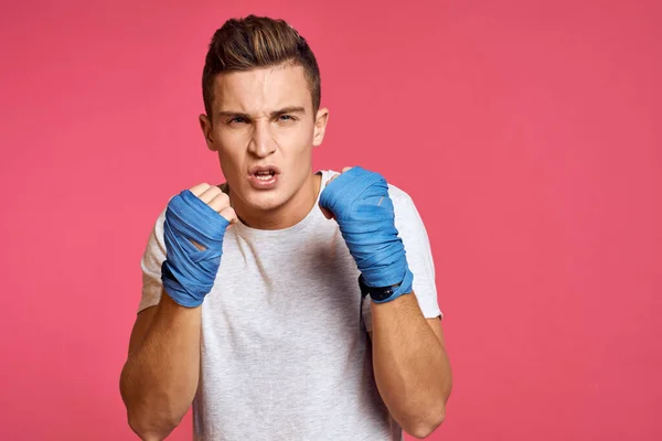 Sportovní muž v modrých boxerských rukavicích a tričku na růžovém pozadí cvičící údery oříznuté pohled — Stock fotografie