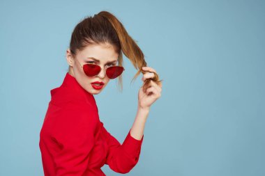 Mavi arka plandaki kırmızı gömlekli kadın yüz ve güneş gözlüklü kırmızı dudak makyajı modeli ile el ele tutuşuyor.