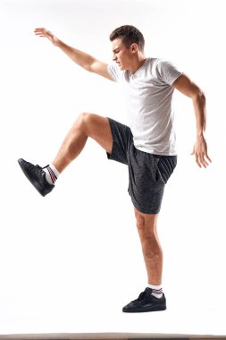 Hafif bir geçmişi olan atletik bir adam tam boy ve koşu şortu spor ayakkabısı tişörtü giyiyor.