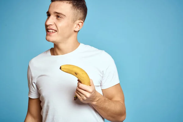 快乐的男人，有着新鲜的水果，手握蓝色背景的白色T恤香蕉 — 图库照片