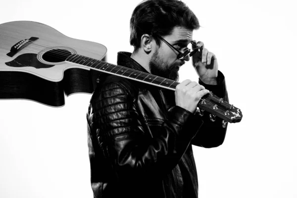 Чоловік тримає гітару в руках музичні емоції чорна шкіряна куртка темні окуляри студійний світлий фон — стокове фото