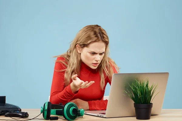 Mujer sentada en una mesa frente a un controlador de auriculares portátiles jugando estilo de vida en línea fondo azul —  Fotos de Stock