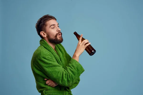 Dronken man in een groene badjas met een fles bier in zijn hand op een blauwe achtergrond alcohol — Stockfoto