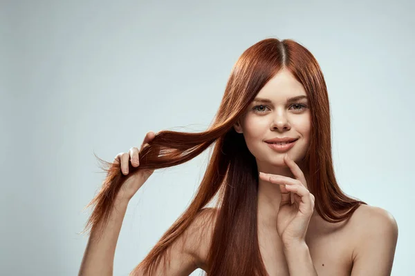 Όμορφη κοκκινομάλλα γυναίκα κρατώντας τα μαλλιά της με τα χέρια περιποίηση γυμνή ώμους φως φόντο — Φωτογραφία Αρχείου