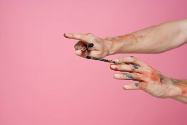 Elleri fırçalı bir adam pembe arka plan hobisi yaratıcı yaklaşımı boyuyor.