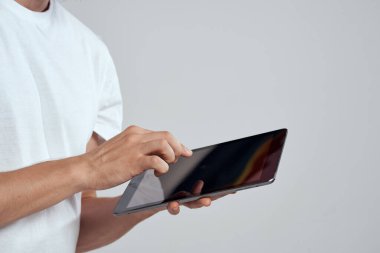 Açık arkaplanda dokunmatik ekranlı tablet erkek elleri beyaz tişört kırpılmış görünüm