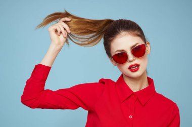 Koyu renk gözlüklü, kırmızı dudaklı, cazibeli stüdyo mavi arka planlı bir kadın.