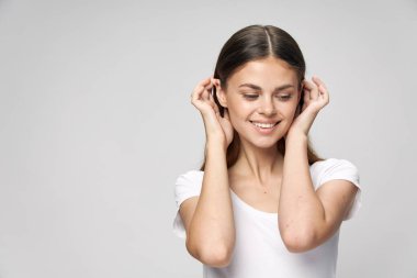 Kadın saçlarını düzeltiyor. Gülümsüyor. Beyaz tişörtünden aşağı bakıyor. 