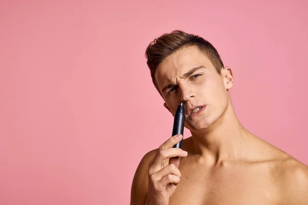 Bello uomo con un trimmer nella sua mano depilazione macchina rosa sfondo nudo torso — Foto Stock