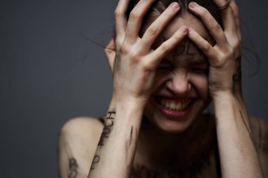 Gri arka planda kırıcı yazılar yazan üzgün kadın elleriyle kendine dokunuyor.