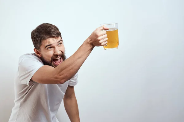 Homem com uma caneca de cerveja em suas mãos e um branco t-shirt luz fundo bigode barba emoções modelo — Fotografia de Stock