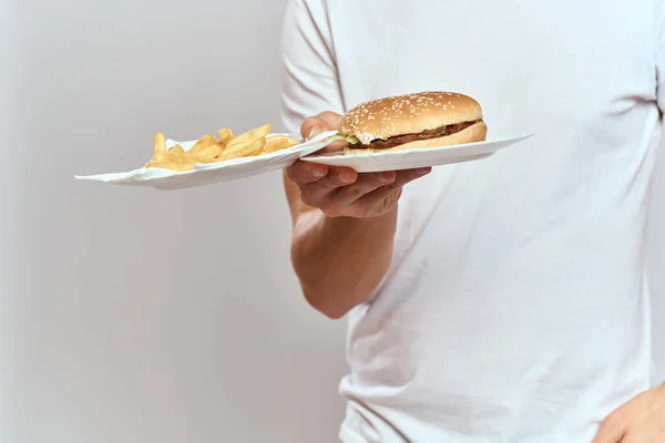 Um homem com batatas fritas e um hambúrguer em um fundo claro em t-shirt branca close-up corte vista Copiar espaço modelo — Fotografia de Stock