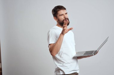 Elinde dizüstü bilgisayarla beyaz tişörtlü bir arka planı olan bir adamın duyguları yeni teknolojileri aydınlatır.