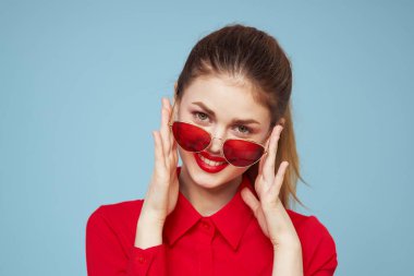 Koyu renk gözlüklü, kırmızı gömlekli, parlak makyajlı çekici bir kadın.