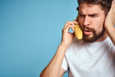 Muzlu bir adam, beyaz bir tişörtle mavi arka planda telefonla iletişim kurarken yakalanır.